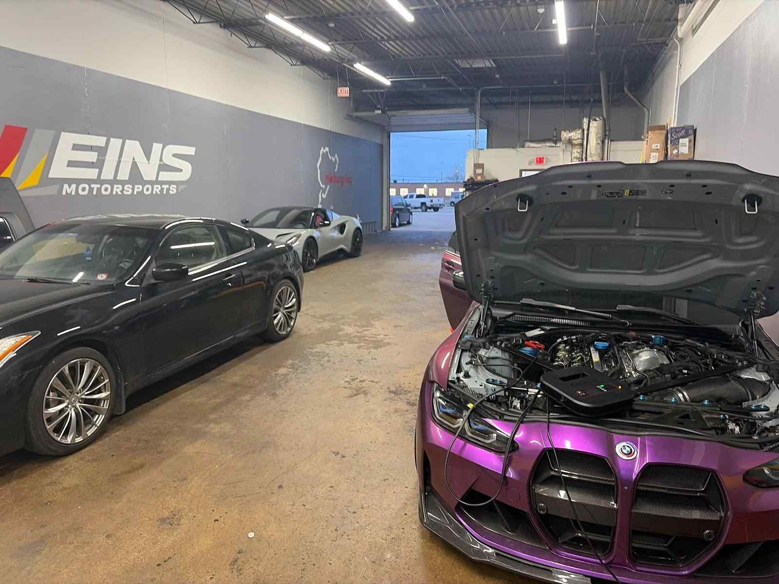 Purple M4 with the hood up in front of the Eins wall