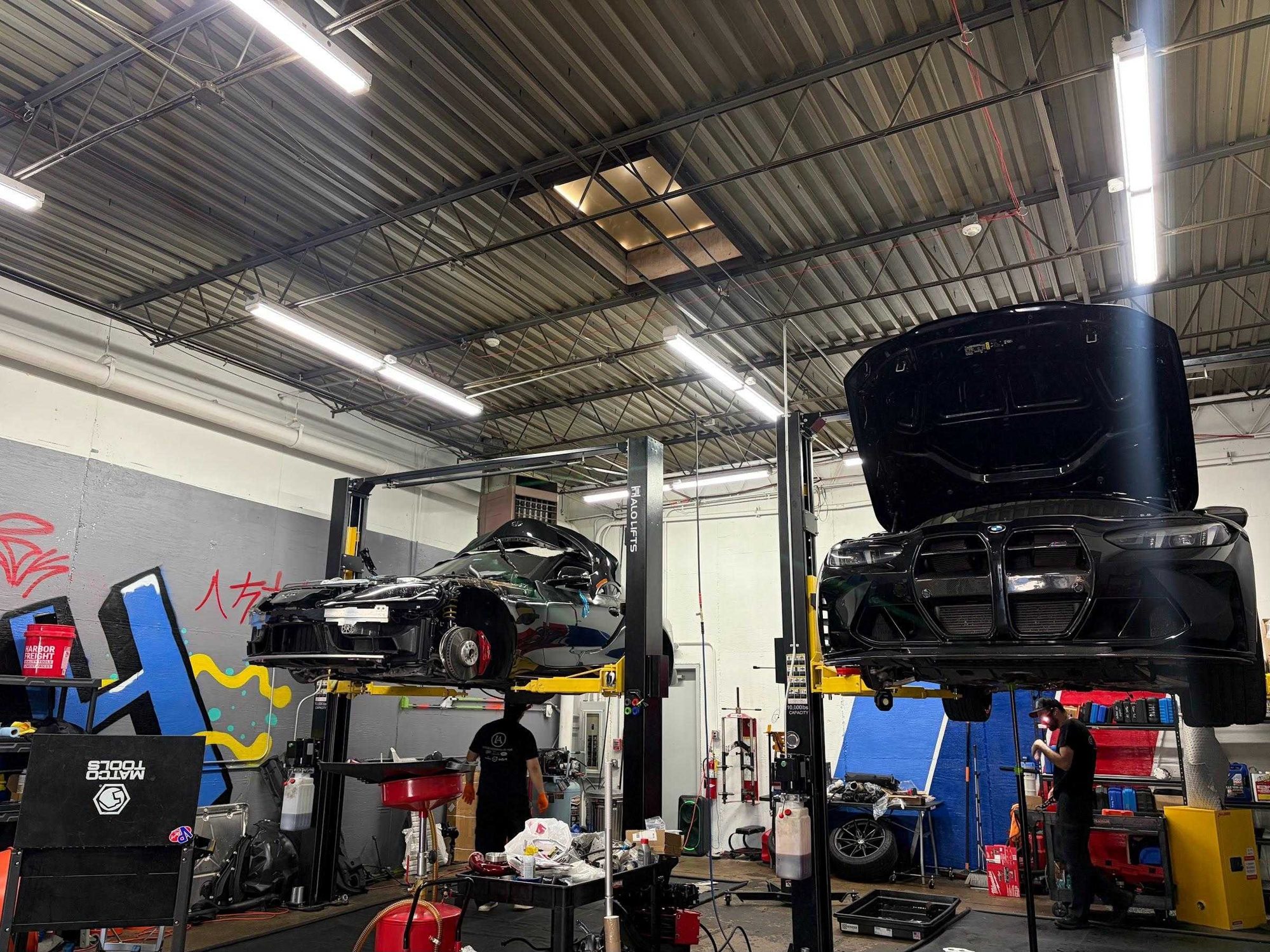 Shop floor: two lifts, cars up, parts laid out below